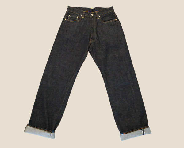 Dark indigo denim jeans with rolled cuffs showing the light blue inner lining, displayed flat against a solid beige background.
