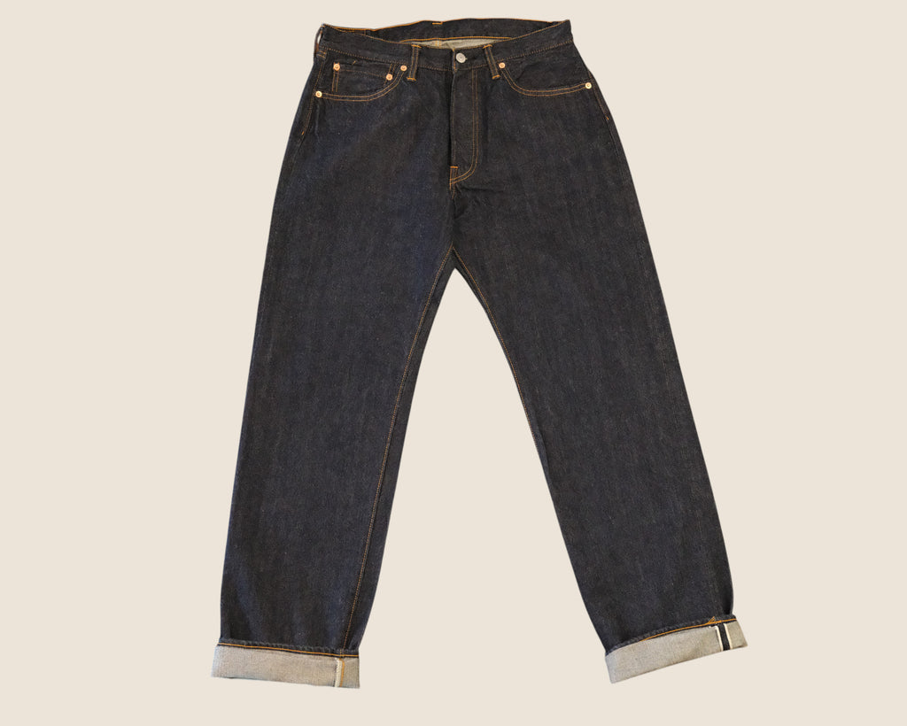 Dark indigo blue denim jeans with rolled cuffs showing a light gray lining, photographed flat against a solid light beige background.