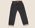 Dark indigo blue denim jeans with rolled cuffs showing a light gray lining, photographed flat against a solid light beige background.