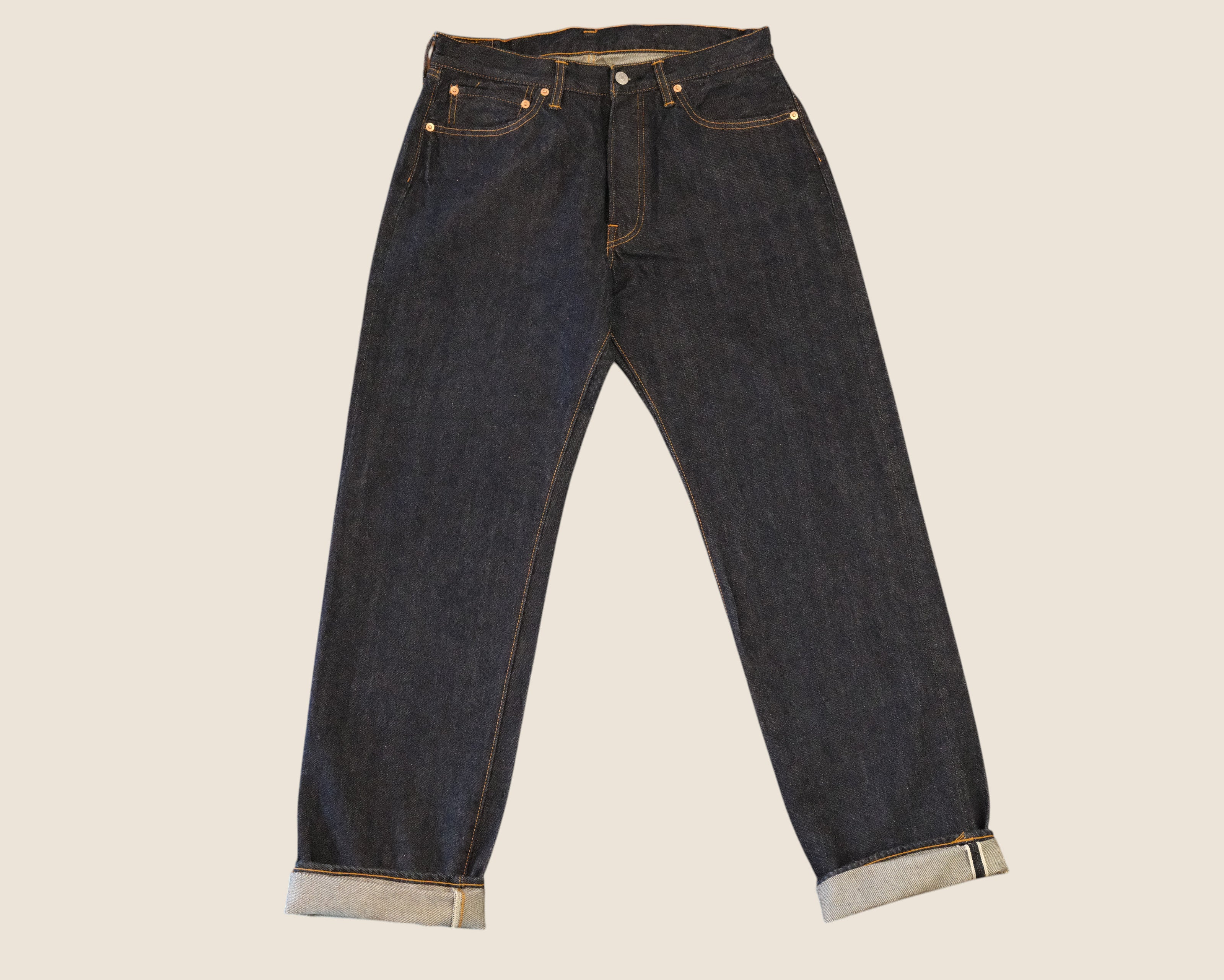 Dark indigo blue denim jeans with rolled cuffs showing a light gray lining, photographed flat against a solid light beige background.