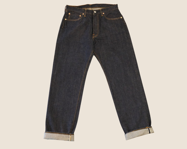 Dark indigo blue denim jeans with rolled cuffs showing a light gray lining, photographed flat against a solid light beige background.
