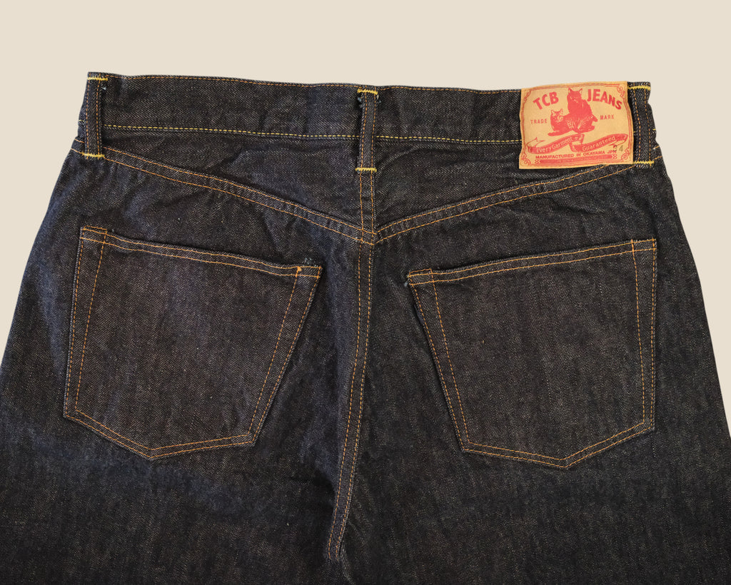 Back view of dark indigo denim jeans showing the waistband, belt loops, and the back pockets with contrast stitching. A red-orange '16C JEANS' brand patch is visible on the upper right side.