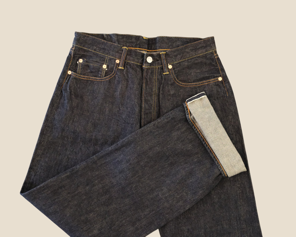 Dark indigo denim jeans folded to show the inner light-wash lining, set against a solid beige background.