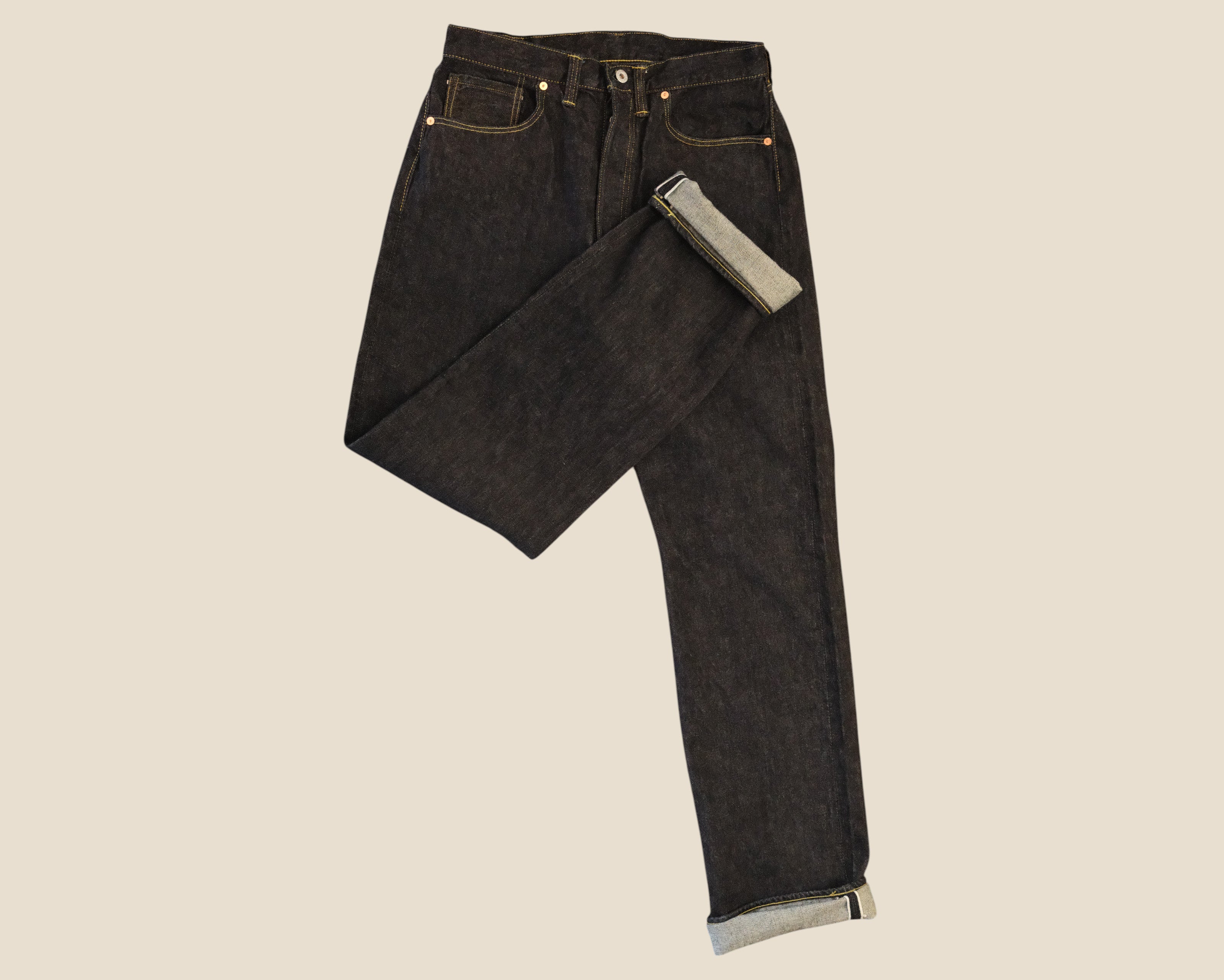 Dark washed black denim jeans with a rolled cuff showing a light gray lining, displayed against a solid beige background.