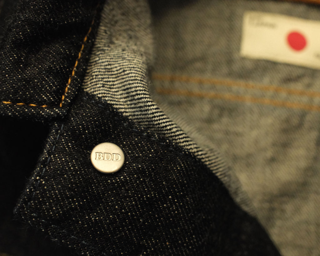 Close-up of a button on denim fabric with a brand label in the background.