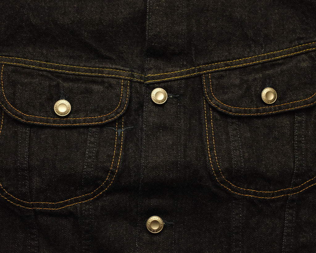 Close-up of a black denim jacket with gold stitching and buttons.