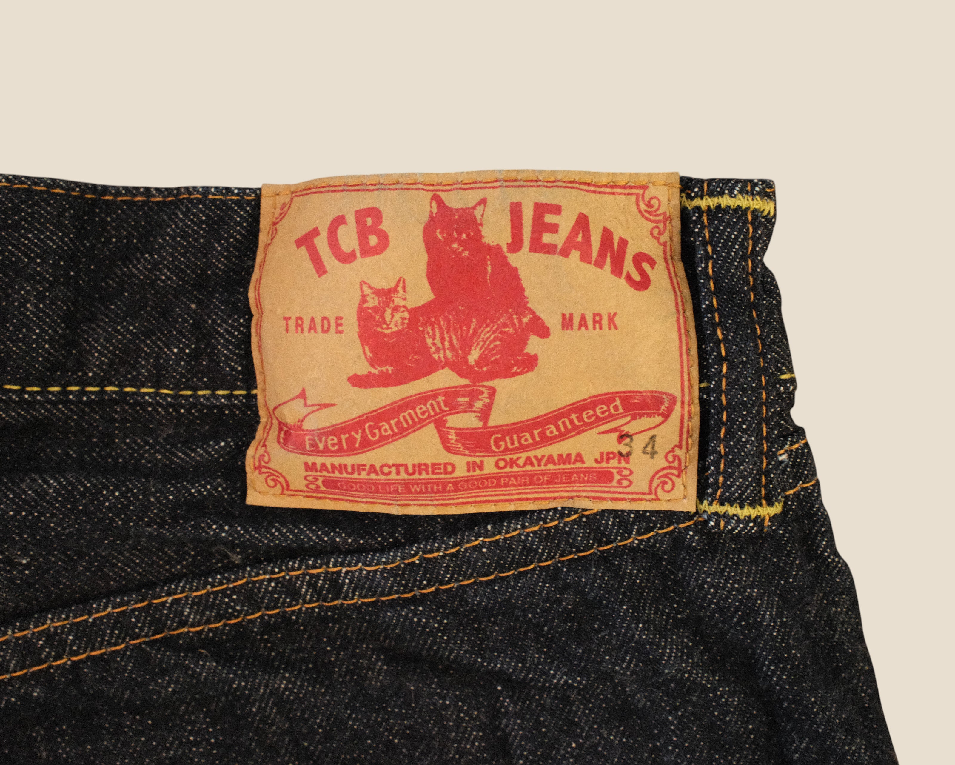 Close-up of the waistband of dark blue denim jeans showing the vintage red and beige TCB Jeans label.